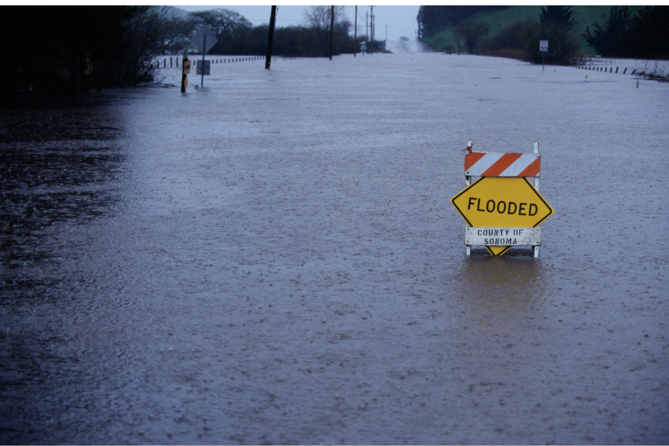 Flooded road in Sonoma County with a 'FLOODED' warning sign standing in water